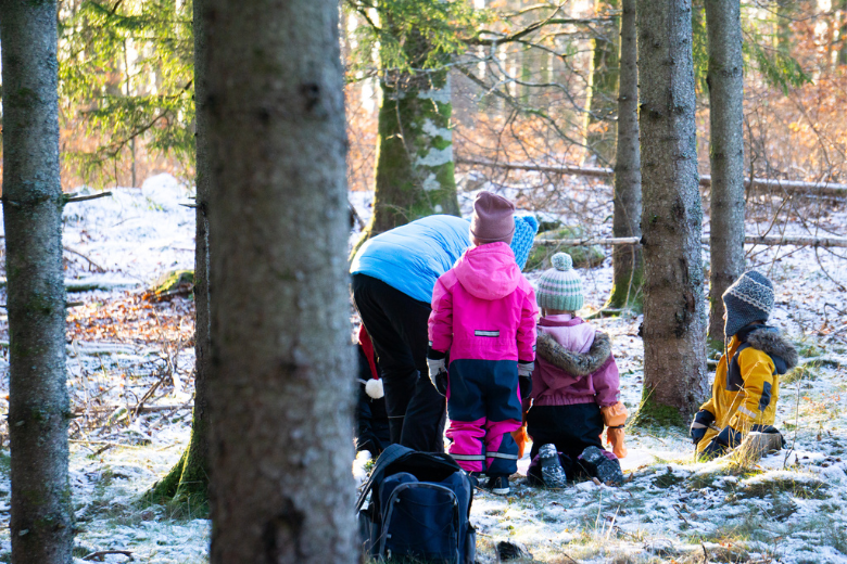 Barn och pedagog sitter i en ring i skogen och pratar