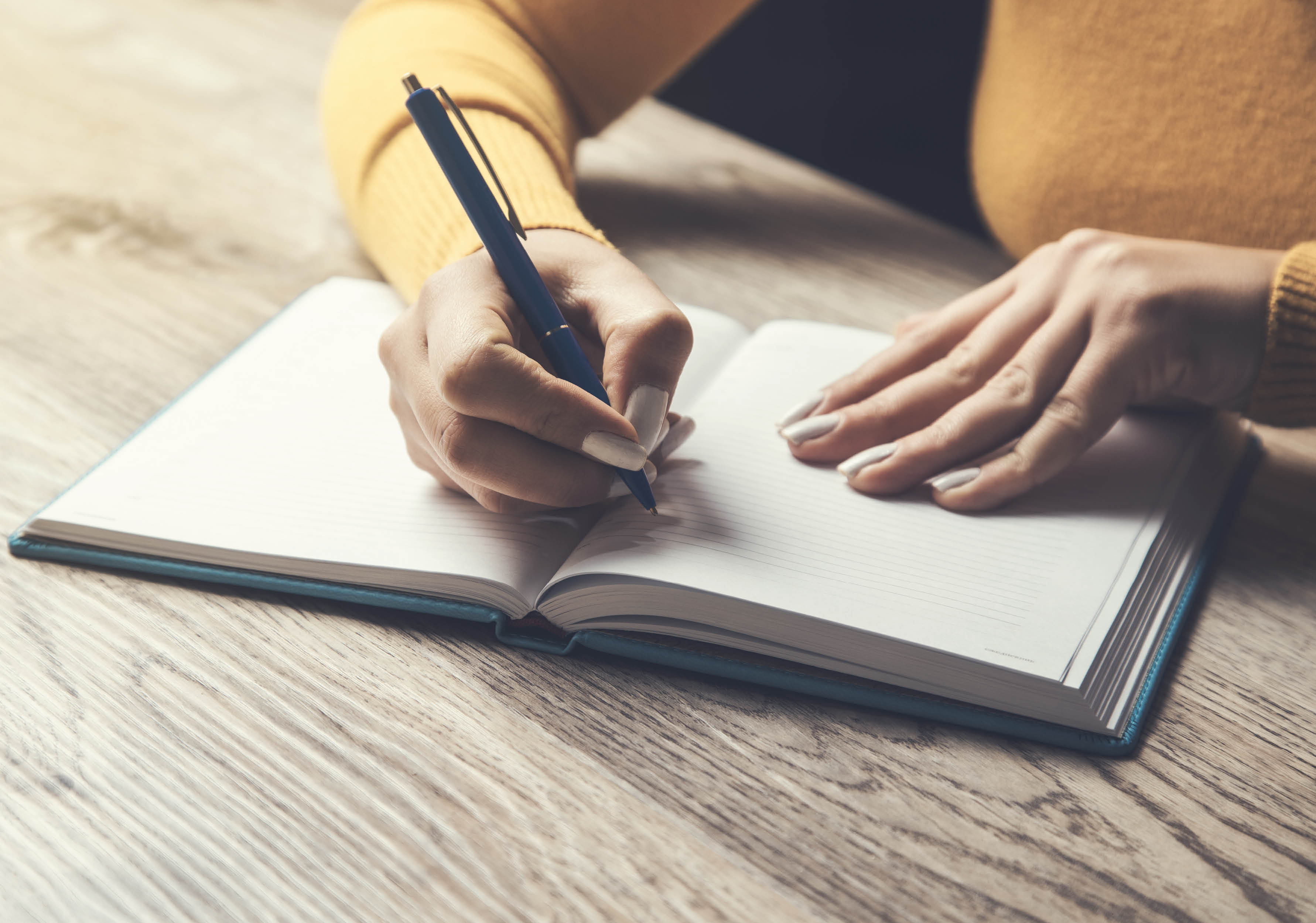 Foto som visar en persons armar och händer, personen håller i en penna och har händerna på en skrivbok och ska börja skriva