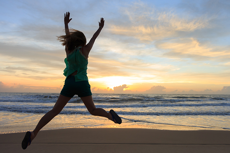 Ung kvinna hoppar på stranden i solnedgången