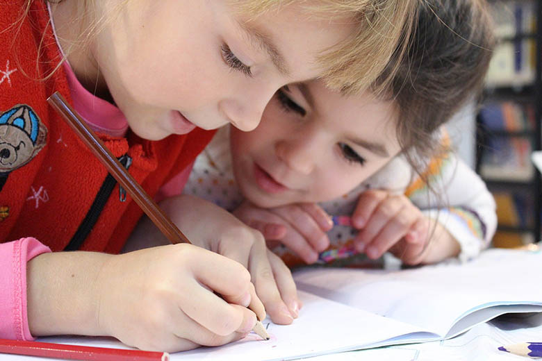 Barn sitter nära varandra och skriver med penna på ett papper.