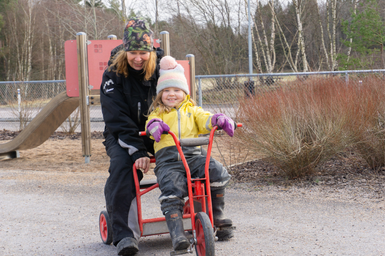 Ibeth och ett barn på uteförskolan sitter tillsammans på en cykel