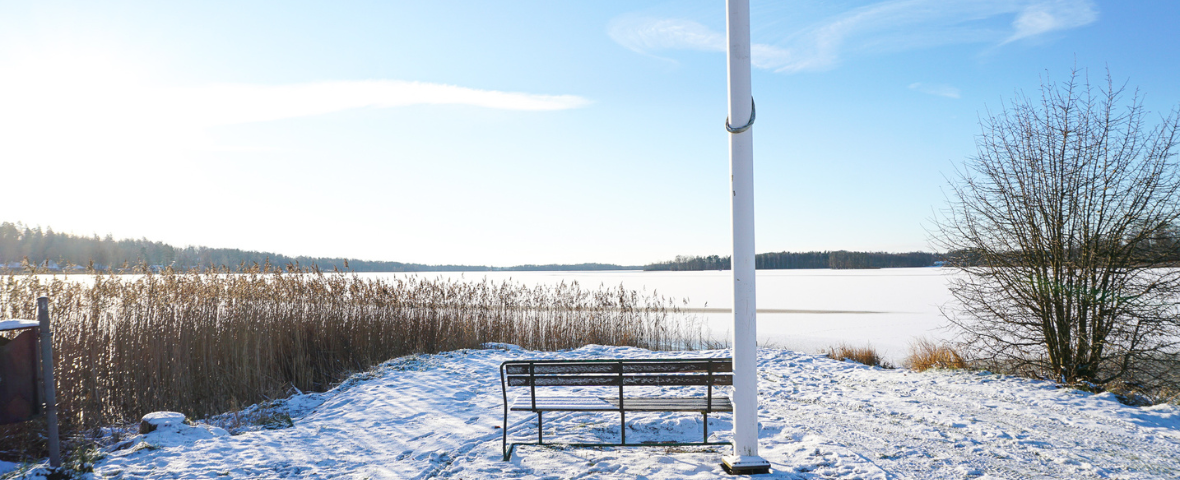 Bänk och flaggstång på Sjöängen med Osbysjön i barkgrunden under vintern